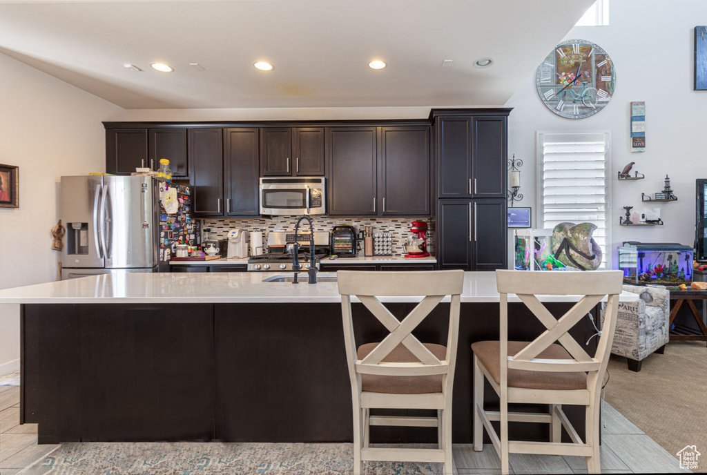 Kitchen with a kitchen island with sink, appliances with stainless steel finishes, backsplash, and light carpet
