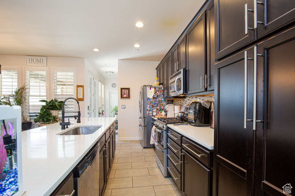 Kitchen with sink, dark brown cabinetry, appliances with stainless steel finishes, and light tile floors