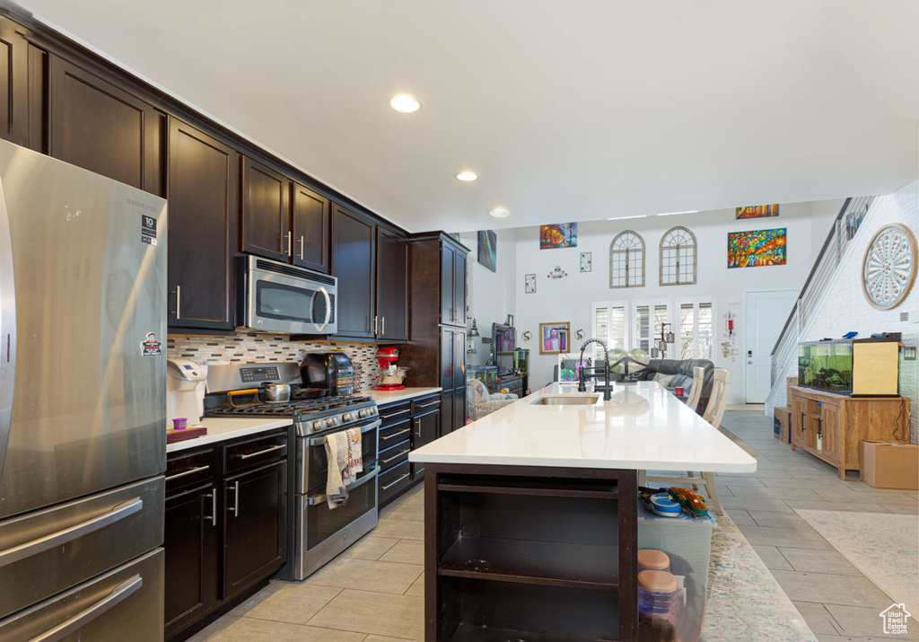 Kitchen featuring light tile flooring, stainless steel appliances, dark brown cabinetry, and backsplash