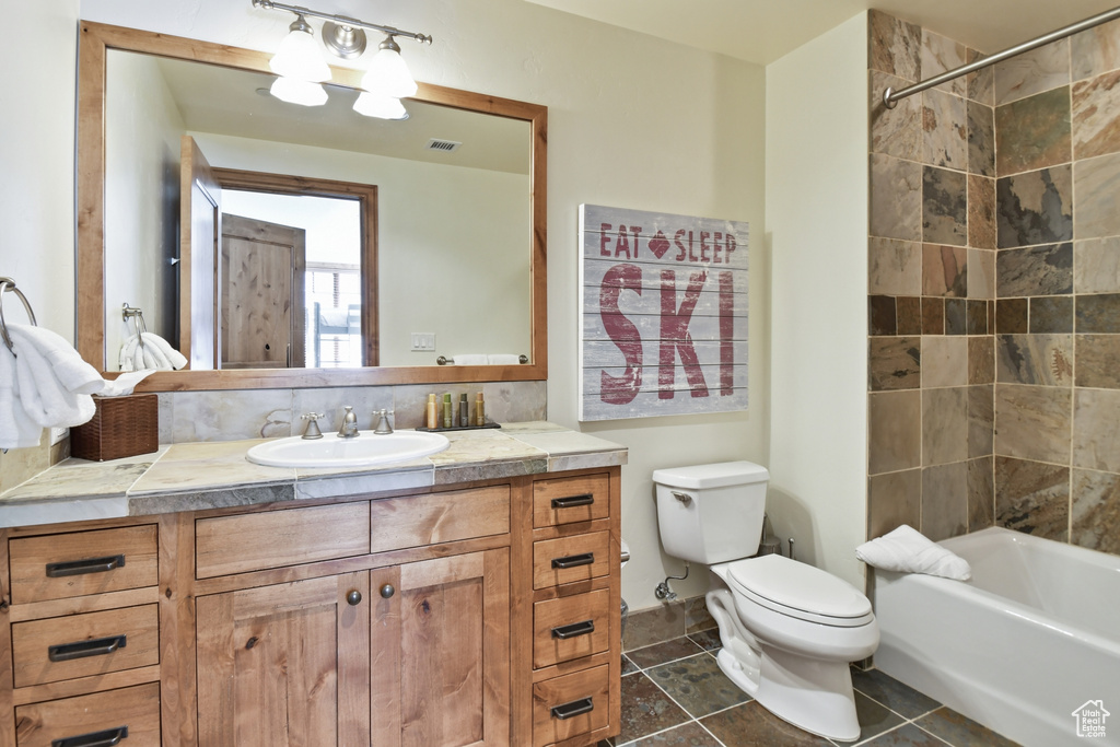 Full bathroom featuring tiled shower / bath combo, tile floors, toilet, and vanity