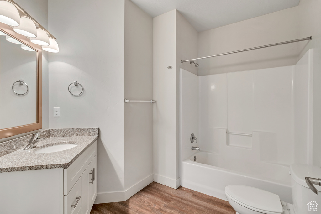 Full bathroom featuring hardwood / wood-style flooring, toilet, vanity with extensive cabinet space, and shower / bathtub combination