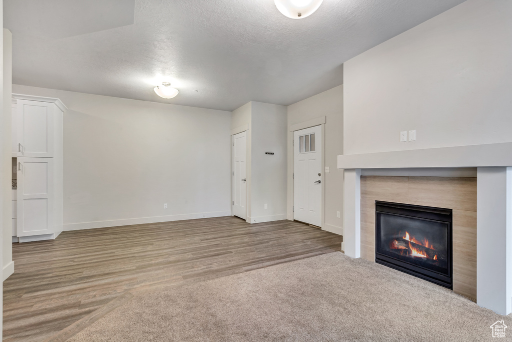 Unfurnished living room with light colored carpet, a textured ceiling, and a tiled fireplace