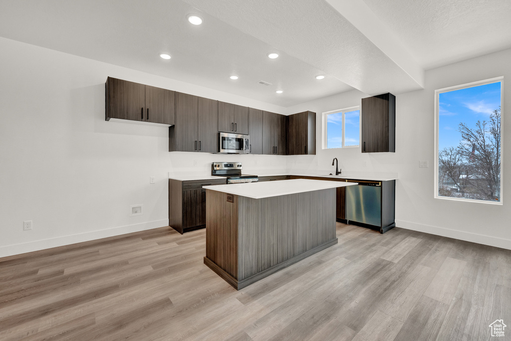 Kitchen featuring appliances with stainless steel finishes, light hardwood / wood-style flooring, a kitchen island, and dark brown cabinets