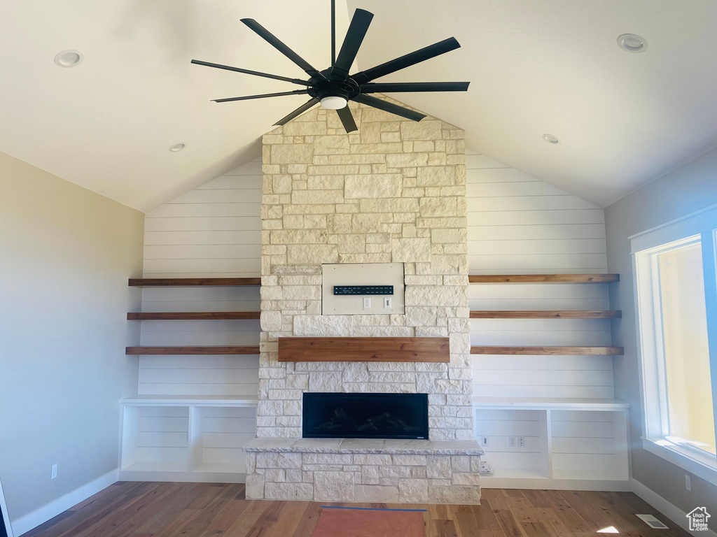 Unfurnished living room with wood-type flooring, ceiling fan, a stone fireplace, and vaulted ceiling