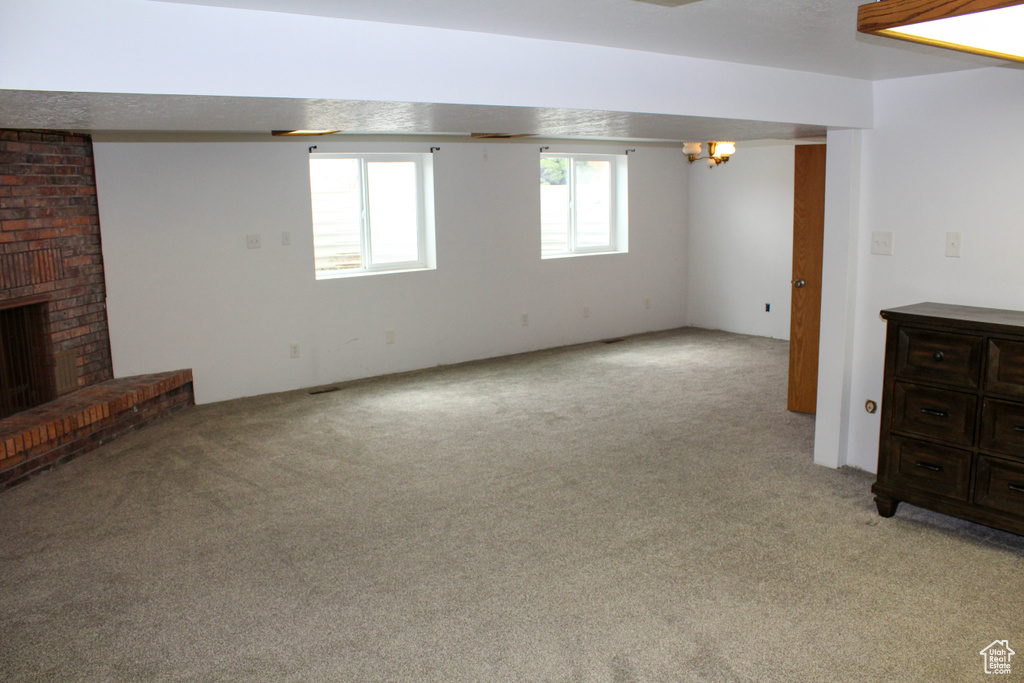 Basement with a brick fireplace, light colored carpet, and brick wall