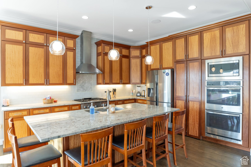 Kitchen with wall chimney exhaust hood, dark wood-type flooring, appliances with stainless steel finishes, a breakfast bar, and pendant lighting