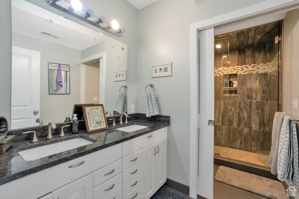 Bathroom with a shower with shower door, tile floors, large vanity, and double sink