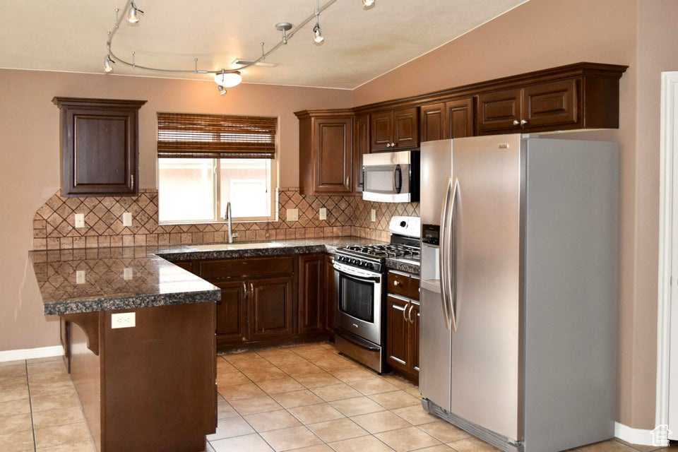 Kitchen featuring sink, rail lighting, light tile floors, backsplash, and stainless steel appliances