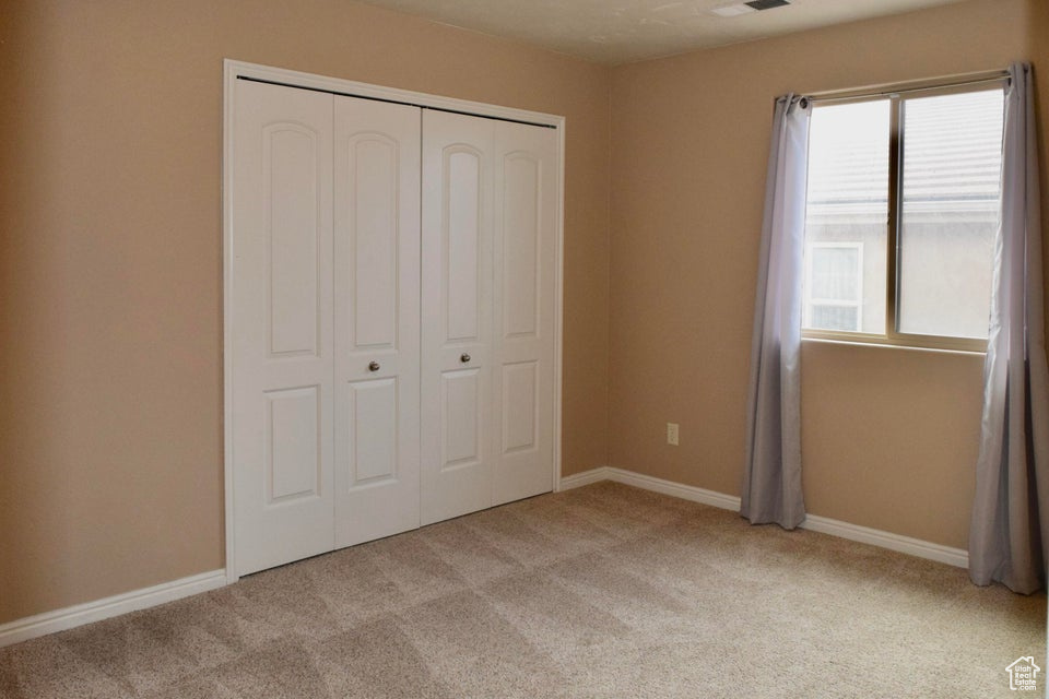 Unfurnished bedroom with multiple windows, light carpet, and a closet