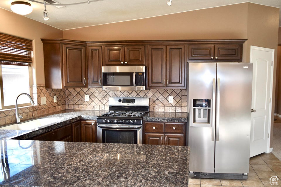 Kitchen with appliances with stainless steel finishes, backsplash, vaulted ceiling, and light tile floors