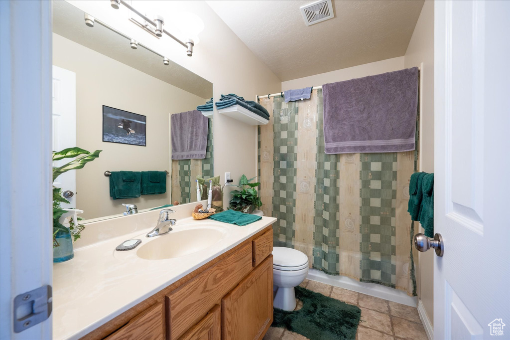 Bathroom featuring a textured ceiling, curtained shower, tile flooring, vanity with extensive cabinet space, and toilet