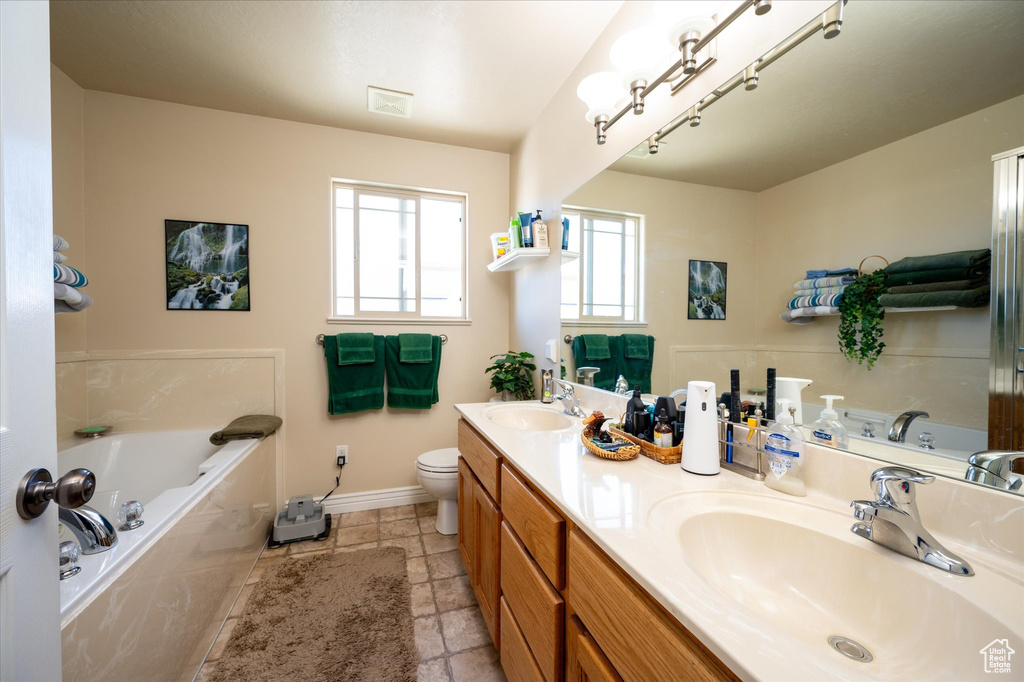 Bathroom featuring dual sinks, tile floors, large vanity, toilet, and a relaxing tiled bath