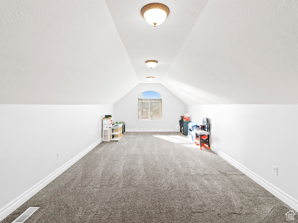 Additional living space with vaulted ceiling and light colored carpet
