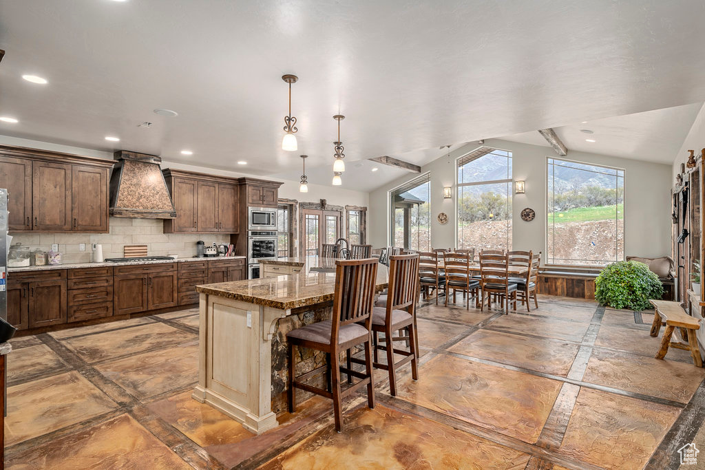 Kitchen with backsplash, custom exhaust hood, a kitchen breakfast bar, stainless steel appliances, and hanging light fixtures