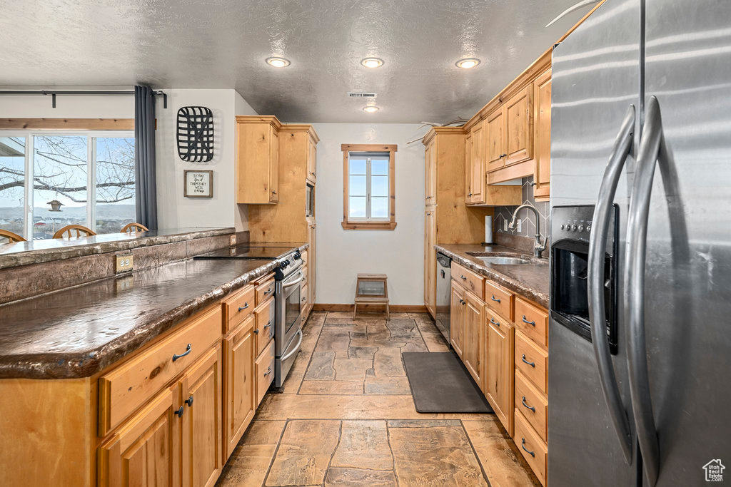 Kitchen featuring a textured ceiling, sink, light tile floors, dark stone countertops, and appliances with stainless steel finishes