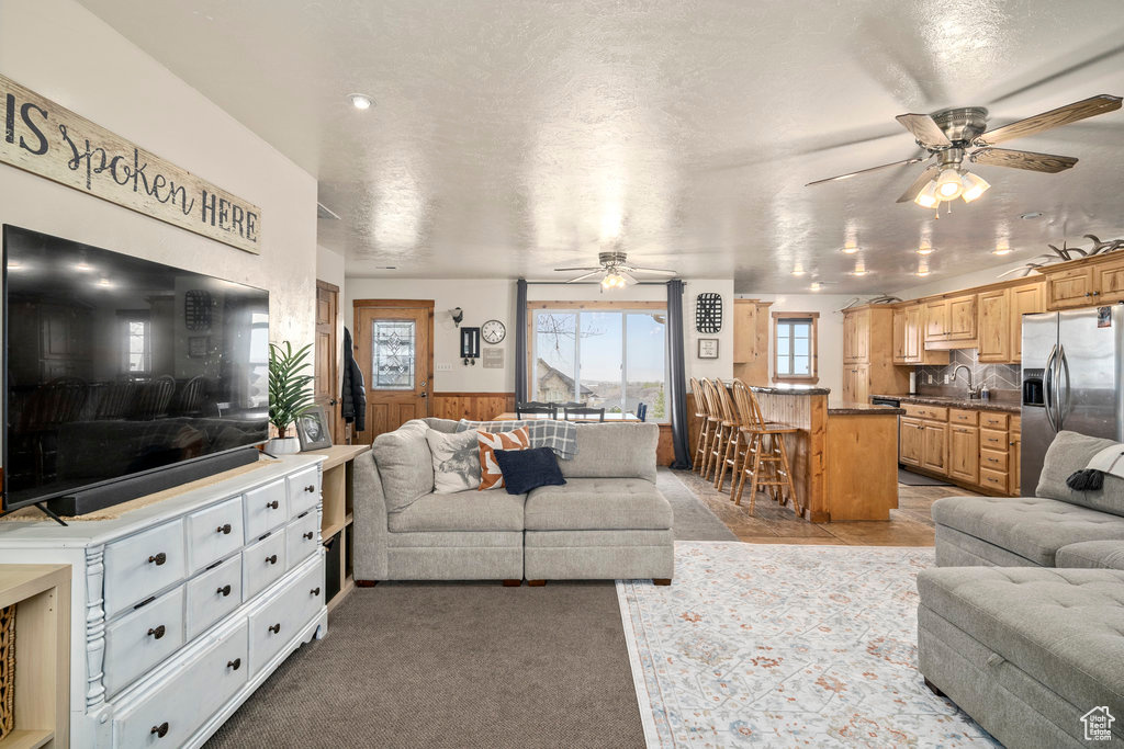 Carpeted living room featuring a textured ceiling, sink, and ceiling fan