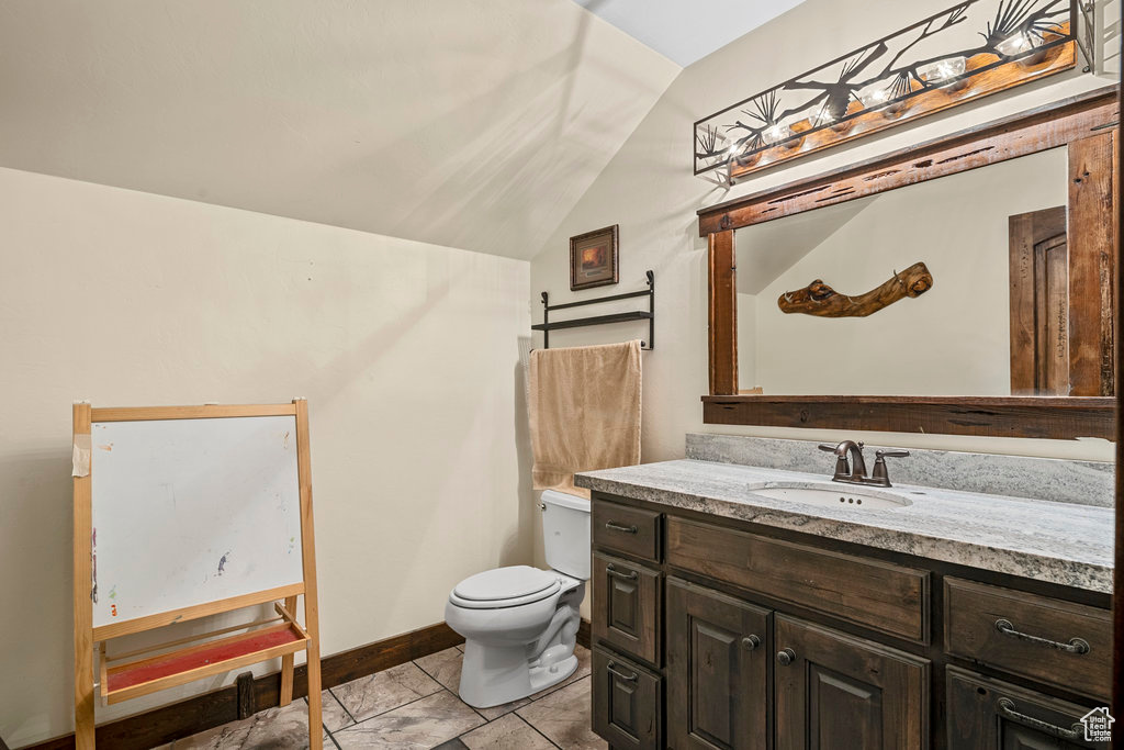 Bathroom featuring vanity, vaulted ceiling, toilet, and tile flooring