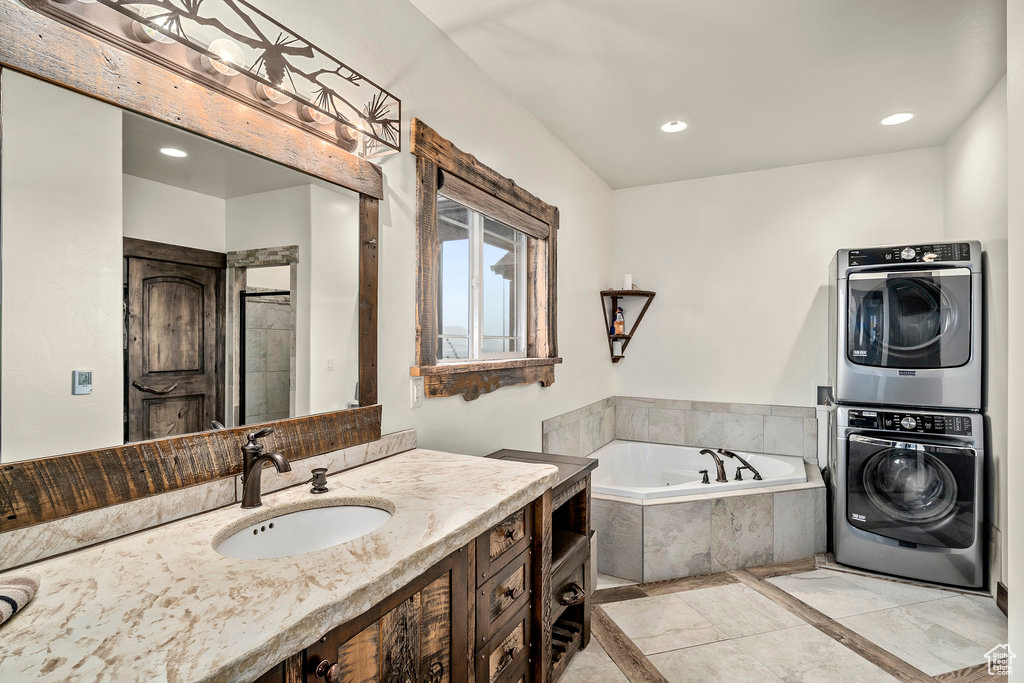 Bathroom featuring stacked washer / drying machine, tile flooring, vanity, and tiled tub