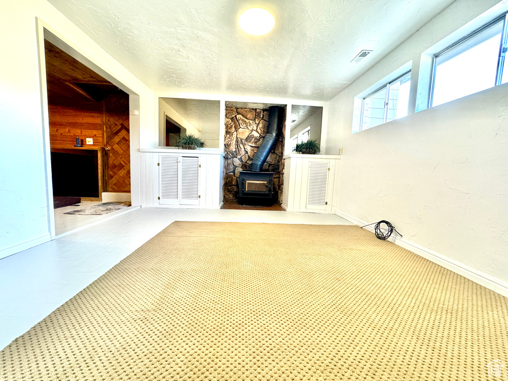 Unfurnished living room with light colored carpet, a wood stove, a textured ceiling, and wood walls