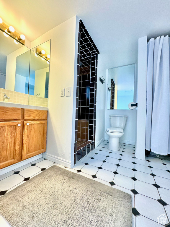Bathroom with tiled shower, vanity, toilet, and tile flooring