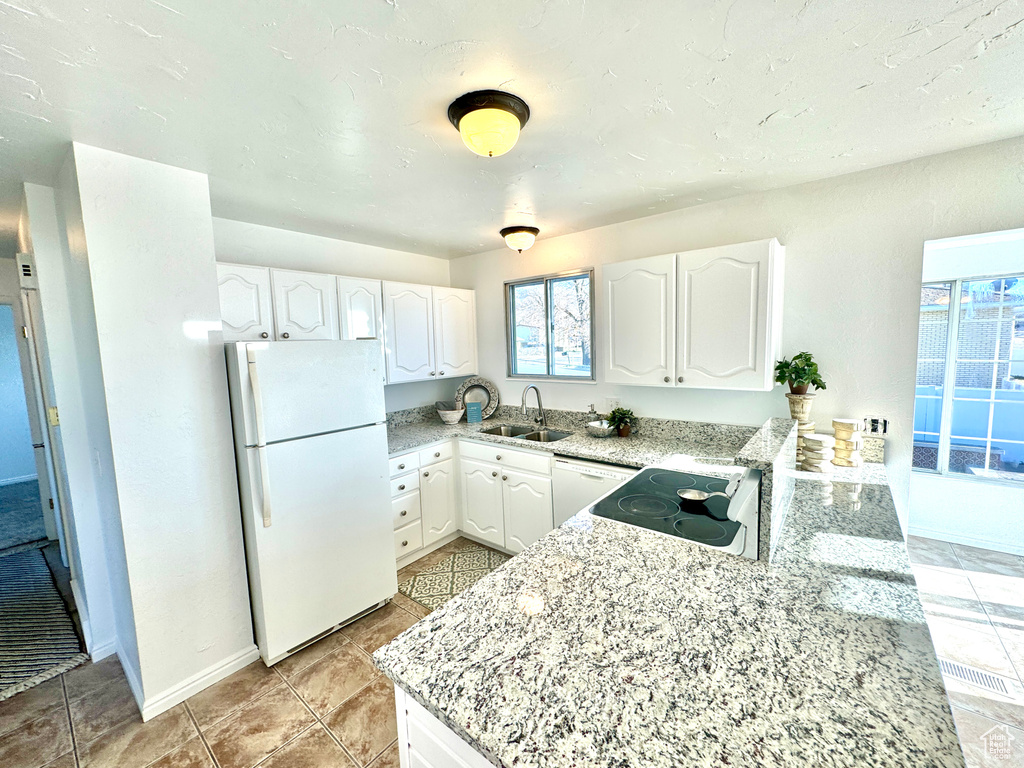 Kitchen featuring white cabinets, light tile floors, white appliances, sink, and light stone countertops