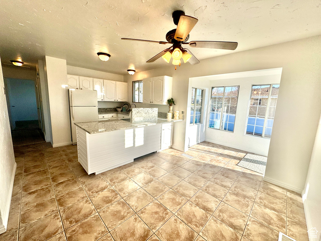 Kitchen featuring light tile floors, ceiling fan, light stone counters, white cabinetry, and white refrigerator