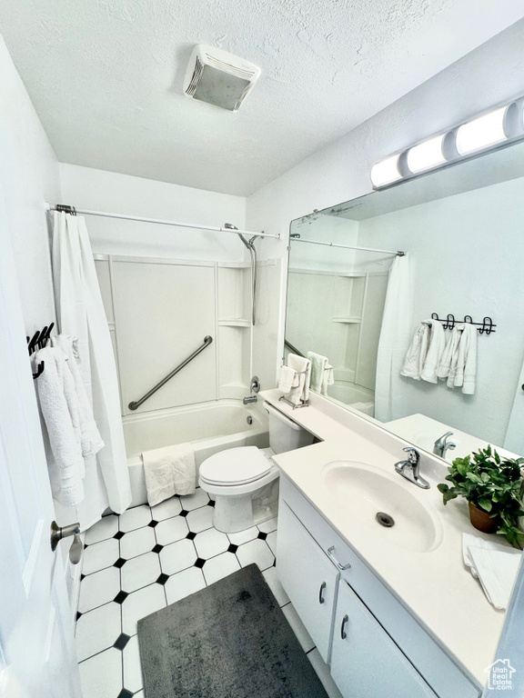 Full bathroom featuring a textured ceiling, large vanity, shower / tub combo with curtain, toilet, and tile flooring