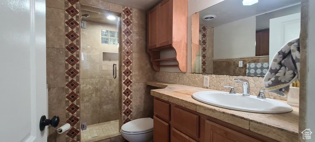 Bathroom with a shower with shower door, tasteful backsplash, tile walls, large vanity, and toilet