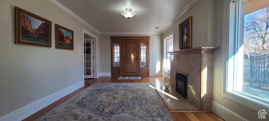 Foyer with dark hardwood / wood-style flooring, a tiled fireplace, and crown molding