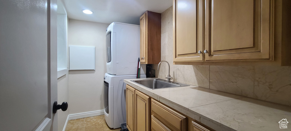 Clothes washing area with stacked washer and clothes dryer, light tile floors, sink, and cabinets