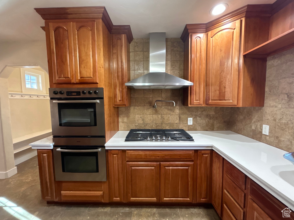 Kitchen featuring appliances with stainless steel finishes, tasteful backsplash, dark tile flooring, and wall chimney range hood