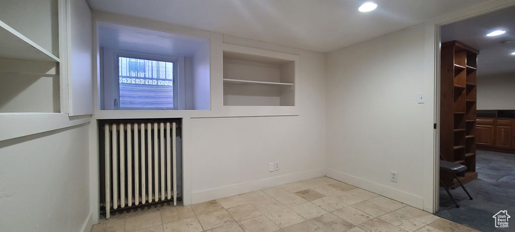 Empty room featuring built in shelves, radiator, and light tile floors