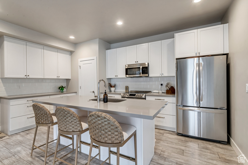 Kitchen featuring a kitchen island with sink, stainless steel appliances, white cabinets, and tasteful backsplash