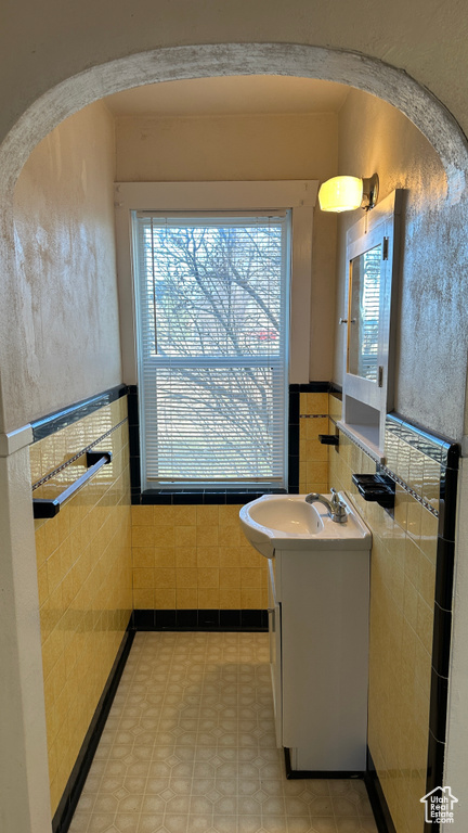 Bathroom with tile flooring, tile walls, vanity, and a healthy amount of sunlight