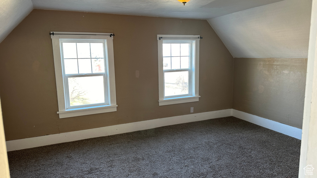 Bonus room featuring plenty of natural light, dark colored carpet, and lofted ceiling