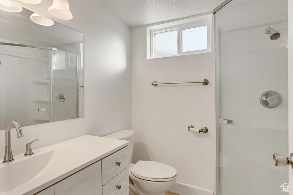 Bathroom with vanity, toilet, a shower with door, and a textured ceiling