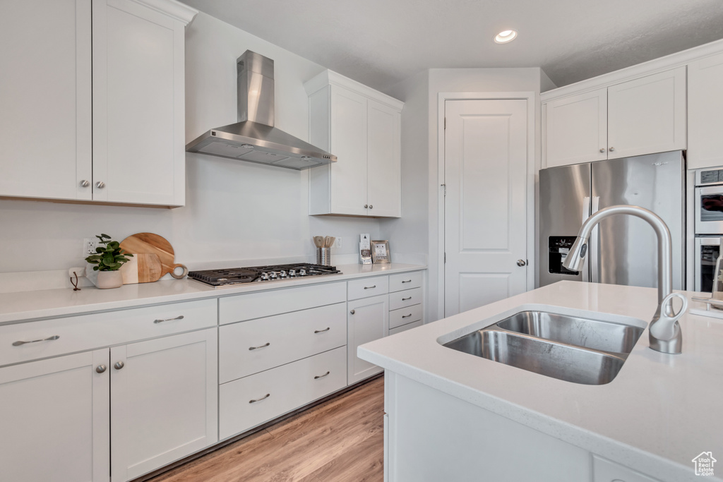 Kitchen featuring white cabinets, appliances with stainless steel finishes, wall chimney range hood, and light hardwood / wood-style floors
