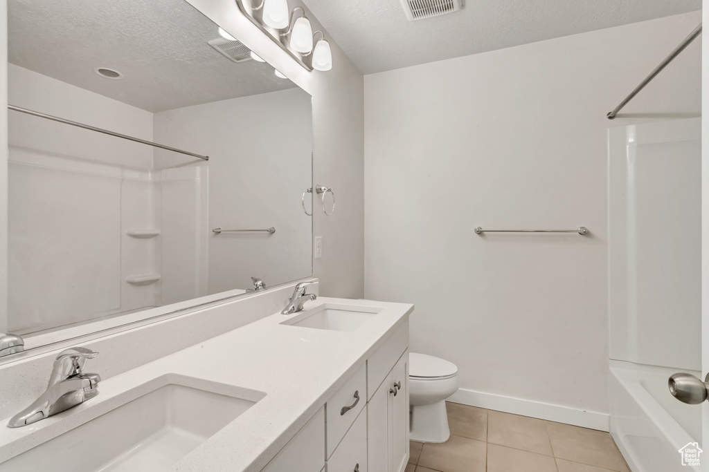 Full bathroom featuring a textured ceiling, bathing tub / shower combination, dual bowl vanity, tile flooring, and toilet