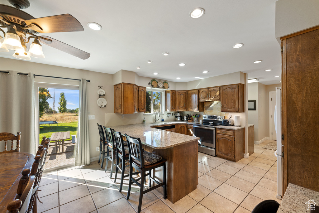 Kitchen featuring a kitchen breakfast bar, light tile flooring, kitchen peninsula, ceiling fan, and stainless steel electric stove
