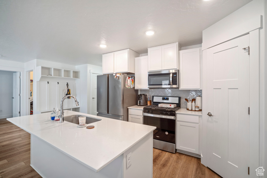 Kitchen featuring sink, an island with sink, light hardwood / wood-style floors, white cabinetry, and stainless steel appliances