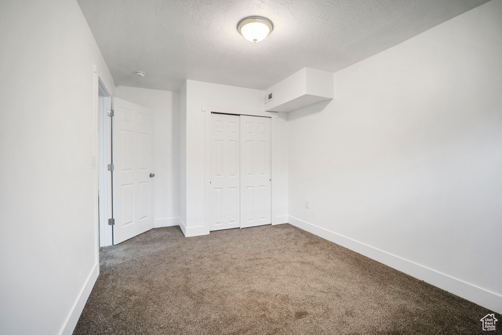 Unfurnished bedroom with a closet, a textured ceiling, and dark carpet