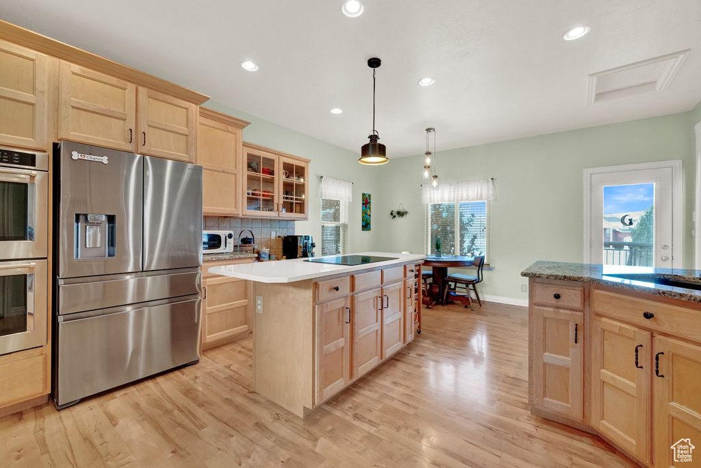 Kitchen with backsplash, light hardwood / wood-style floors, a center island, stainless steel appliances, and pendant lighting