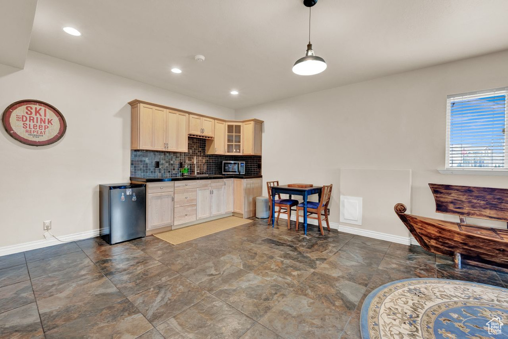 Kitchen with dark tile flooring, light brown cabinetry, tasteful backsplash, hanging light fixtures, and fridge