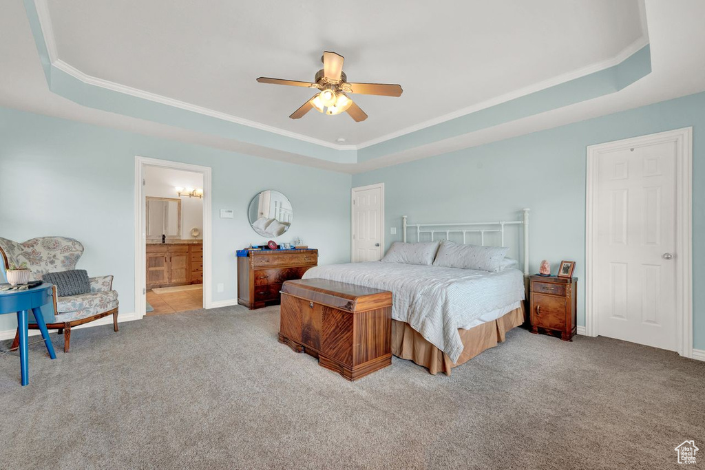 Bedroom featuring a raised ceiling, ensuite bathroom, light carpet, ornamental molding, and ceiling fan