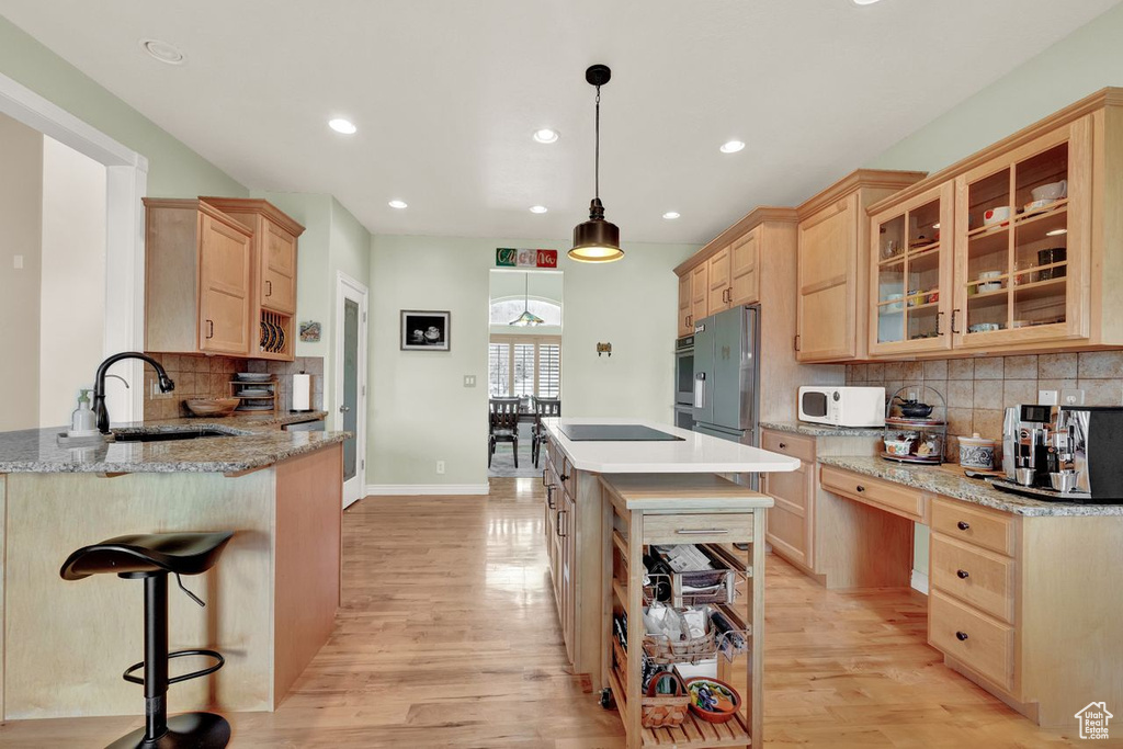 Kitchen featuring decorative light fixtures, tasteful backsplash, stainless steel appliances, and light hardwood / wood-style floors
