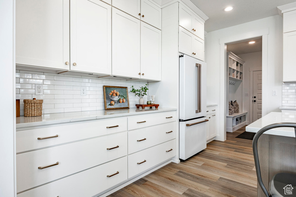 Kitchen featuring high end white refrigerator, tasteful backsplash, white cabinetry, and light hardwood / wood-style flooring