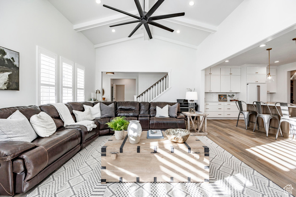 Living room featuring beamed ceiling, high vaulted ceiling, ceiling fan, and light wood-type flooring