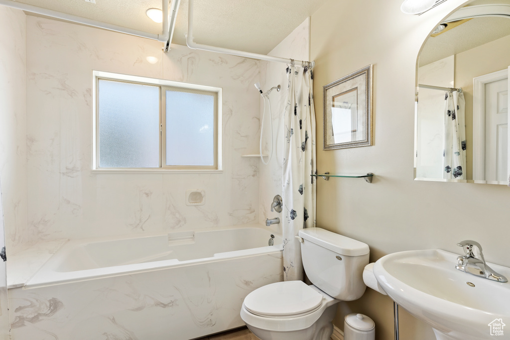 Full bathroom with toilet, shower / bath combination with curtain, a textured ceiling, and sink