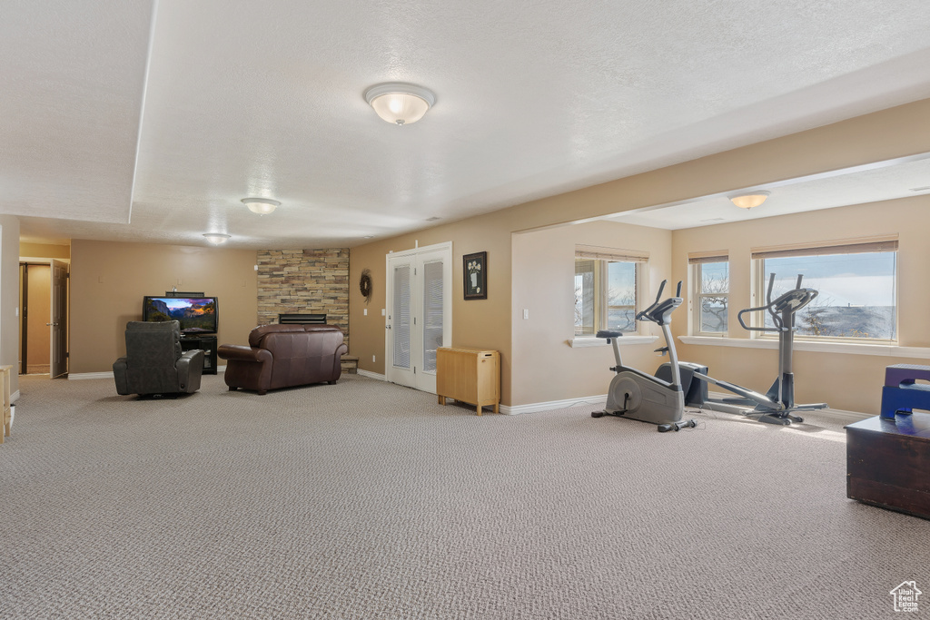 Exercise area featuring a stone fireplace, french doors, and light carpet