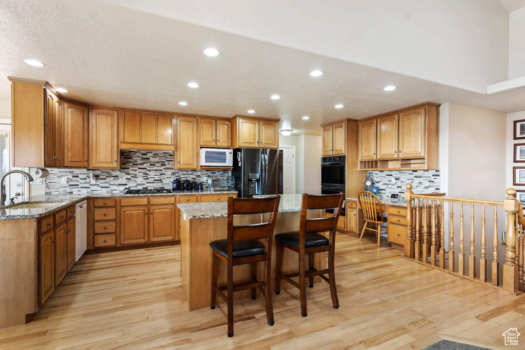 Kitchen featuring sink, light wood-type flooring, stainless steel appliances, and light stone countertops